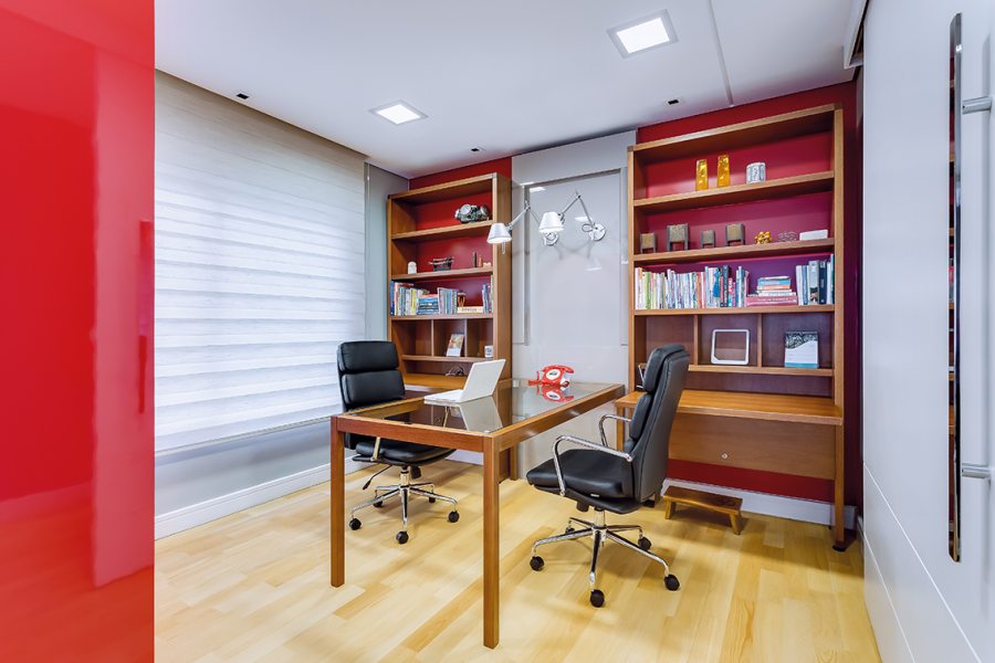 O escritório possui mesa que acomoda duas pessoas, iluminação com spots de embutir e arandelas (Grey House Iluminação) e mobiliário com nichos em laca colorida