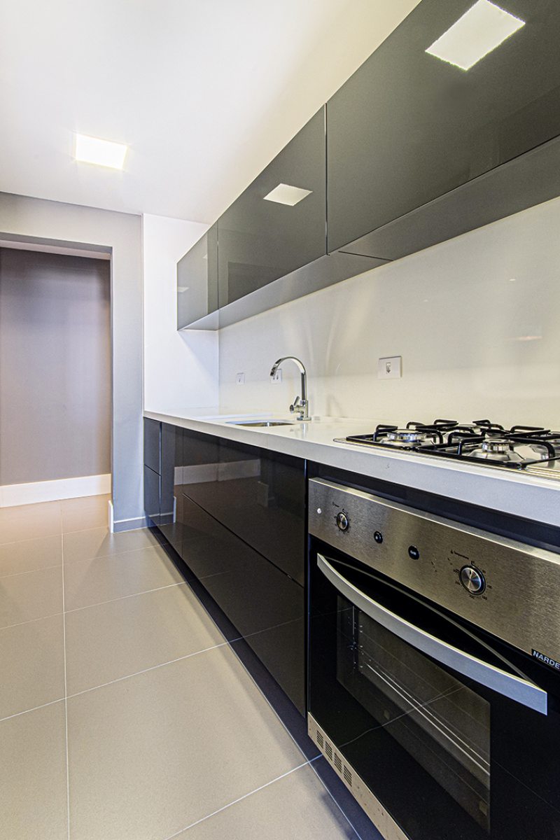 Tanto na lavanderia quanto na cozinha, os armários em cores escuras (Todeschini Batel) possuem portas em pintura alto brilho e tampos em pedra branca que contrastam entre si