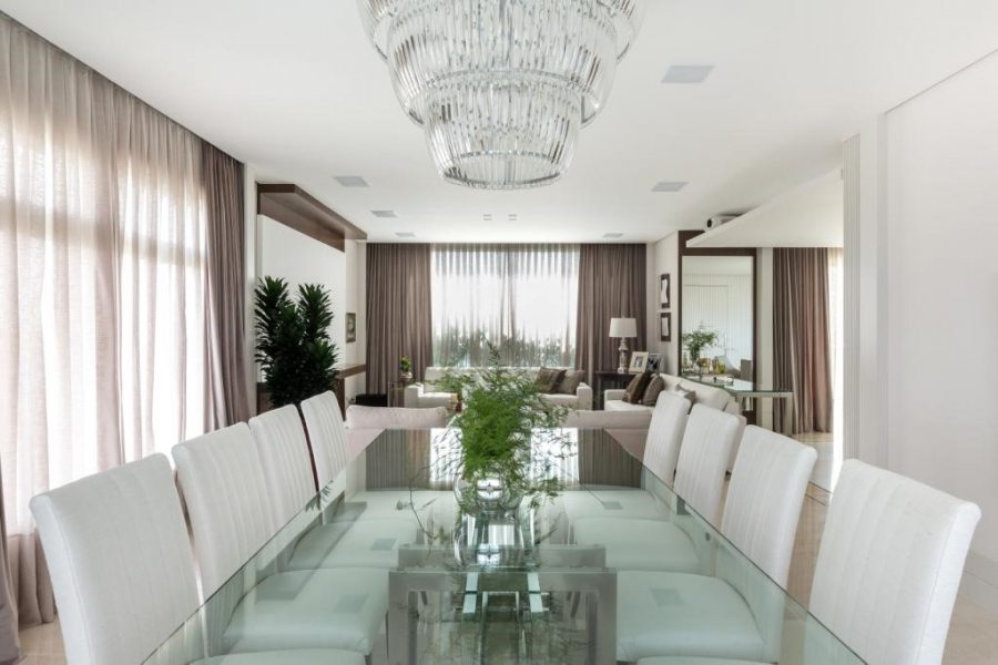 A sala de jantar, integrada ao living, possui mesa de vidro com base em aço inox e cadeiras da Sierra Curitiba em seda rústica branca