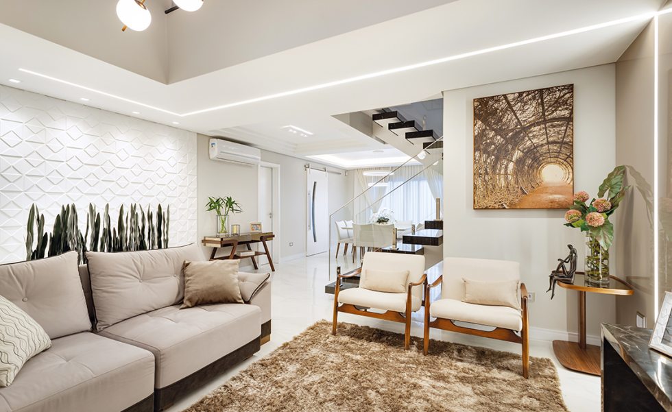 Na sala de estar, a cortina de pé direito duplo (M. Decor) se destaca com as luminárias pendentes de hastes metálicas na cor bronze. Na sala de estar, a cortina de pé direito duplo (M. Decor) se destaca com as luminárias pendentes de hastes metálicas na cor bronze.