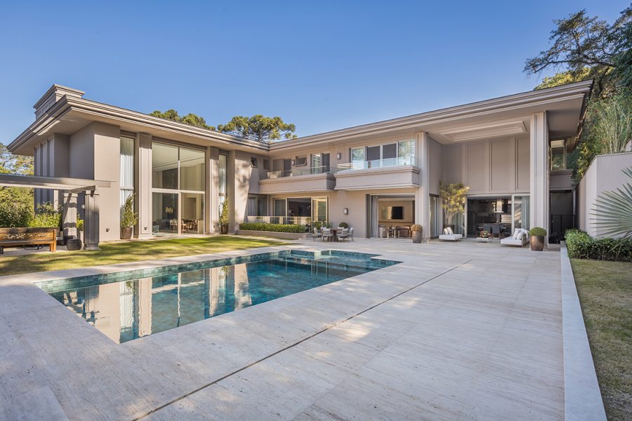 A piscina externa com área de lazer integrada atendeu ao desejo do casal de usufruir de uma estrutura completa para curtir junto aos filhos e manter a saúde em dia. A residência foi distribuída em três setores distintos a fim de acomodar o extenso programa de necessidades dos moradores. O layout em “L”, alongado na lateral esquerda, conectou a área social à lateral ensolarada em meio a um bosque preservado