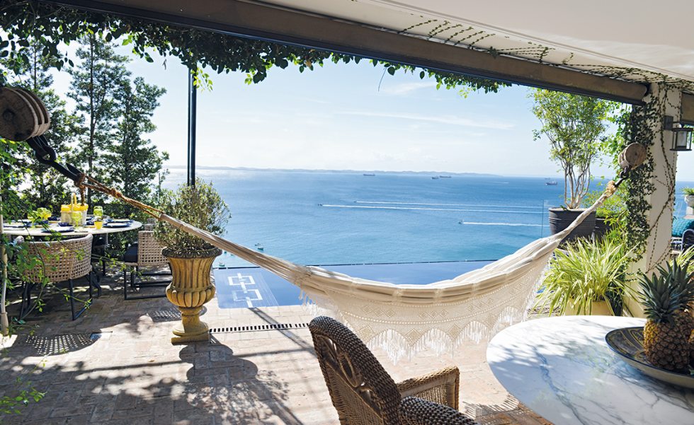 A área da piscina de borda infinita e vista para o mar possui gazebo trabalhado em ferro, vasos em estilo clássico e mobiliário próprio para área externa A área da piscina de borda infinita e vista para o mar possui gazebo trabalhado em ferro, vasos em estilo clássico e mobiliário próprio para área externa