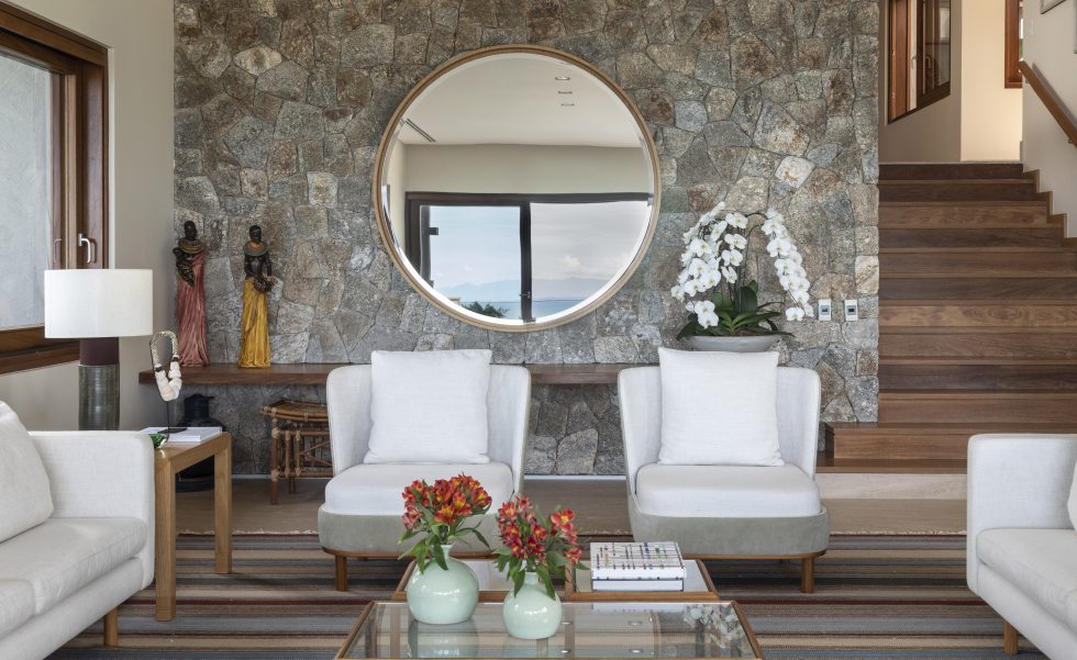 O grande espelho redondo compõe a parede deste living que foi revestida com a atmosfera rústica da pedra moledo | Projeto do escritório Corradi Mello Arquitetura | Foto: Evelyn Müller O grande espelho redondo compõe a parede deste living que foi revestida com a atmosfera rústica da pedra moledo | Projeto do escritório Corradi Mello Arquitetura | Foto: Evelyn Müller
