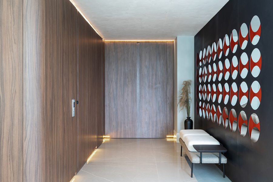 No hall, a madeira escura aparece em painéis e mobiliários, compondo com a iluminação indireta e o mobiliário pontual uma ambientação de transição entre o exterior e a área social.