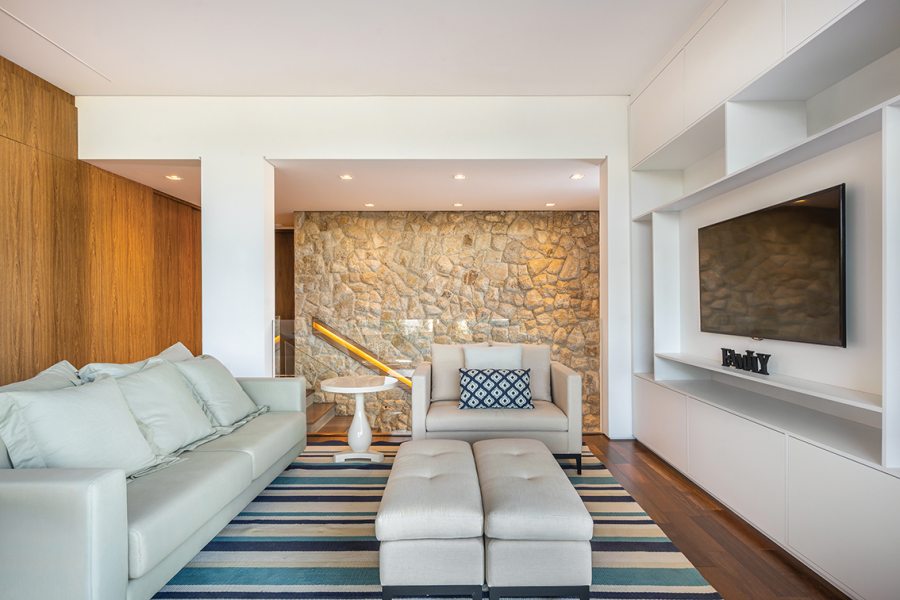 O décor da sala de TV, com piso de madeira maciça da Maderatto, ganhou personalidade a partir do tapete listrado em nuances de azul e da almofada com padrão geométrico em mesmo tom