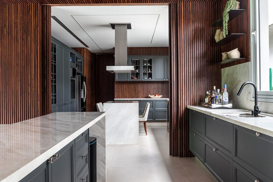 A cozinha com ilha central de mármore ganhou marcenaria sob medida com portas de laca cinza e puxadores inox. As portas de correr permitem integrar cozinha e gourmet ou separá-los, dependendo da ocasião.