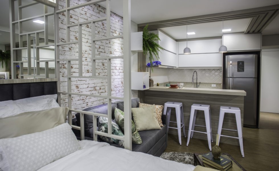 Uma divisória em MDF com desenho geométrico personalizado separa sutilmente o living do quarto. No estar, o sofá cama foi feito sob medida em tecido acamurçado cinza Uma divisória em MDF com desenho geométrico personalizado separa sutilmente o living do quarto. No estar, o sofá cama foi feito sob medida em tecido acamurçado cinza