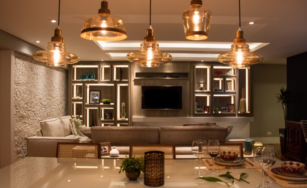 A sala de estar com lareira e home theater, ao fundo, possui estante trabalhada com MDF Linheiro Griggio (Arauco) e fitas de LED embutidas nos vãos da estrutura do móvel, executado pela GMK Marcenaria A sala de estar com lareira e home theater, ao fundo, possui estante trabalhada com MDF Linheiro Griggio (Arauco) e fitas de LED embutidas nos vãos da estrutura do móvel, executado pela GMK Marcenaria