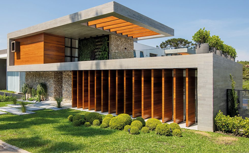 A fachada da casa é contemporânea e trabalhada com linhas retas horizontais. O acesso principal possui paredes revestidas com pedra moledo, para contrastar com a textura do concreto ripado e da madeira cumaru