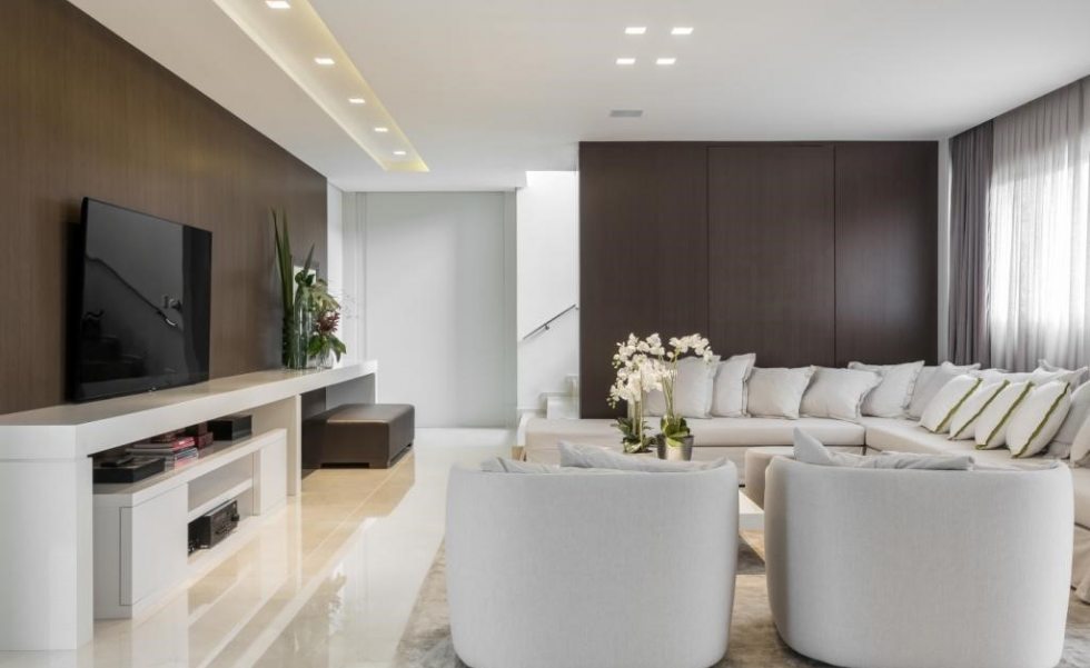 O piso térreo abriga a sala íntima da família, com living, espaço para jogos e brinquedoteca integrada com gourmet e escritório. Uma longilínea bancada em Caesarstone branco ocupa toda a extensão de uma das paredes, funcionando como aparador para a TV e apoio para a área de circulação e acesso ao piso superior O piso térreo abriga a sala íntima da família, com living, espaço para jogos e brinquedoteca integrada com gourmet e escritório. Uma longilínea bancada em Caesarstone branco ocupa toda a extensão de uma das paredes, funcionando como aparador para a TV e apoio para a área de circulação e acesso ao piso superior