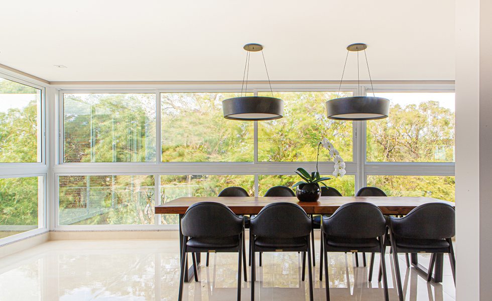 Integrada ao espaço gourmet, a sala de jantar possui vista para a natureza exuberante do entorno. A mesa de madeira de demolição e o mobiliário de cores escuras contrasta com a ampla luminosidade natural Integrada ao espaço gourmet, a sala de jantar possui vista para a natureza exuberante do entorno. A mesa de madeira de demolição e o mobiliário de cores escuras contrasta com a ampla luminosidade natural