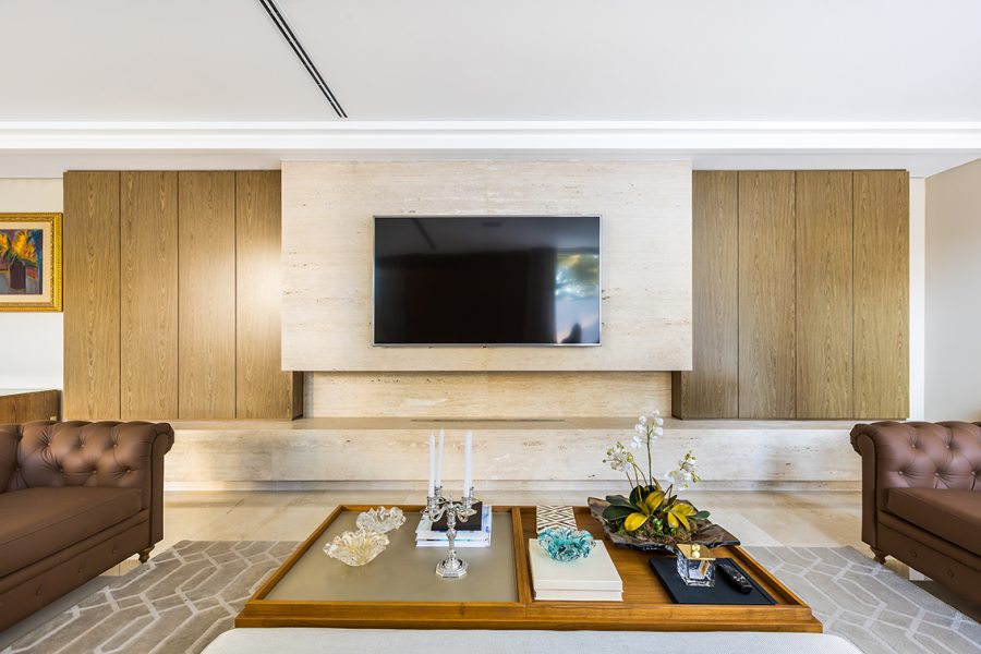 Painéis de madeira, espelhos e acabamentos metalizados compõem o décor sofisticado da sala de TV com lareira