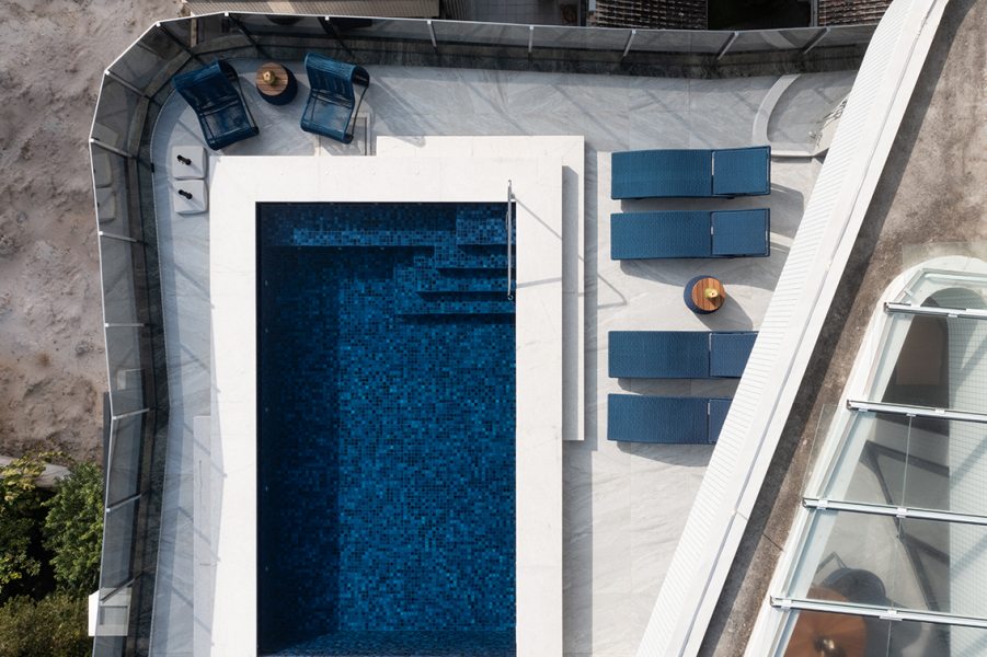 A arquitetura do edifício da Construtora Golpar priorizou a fluidez entre os ambientes internos e externos. A área social superior se abre completamente para o deck com piscina. Vista de outro ângulo, a piscina e o mobiliário em tons de azul remetem à vista privilegiada para a paisagem litorânea.