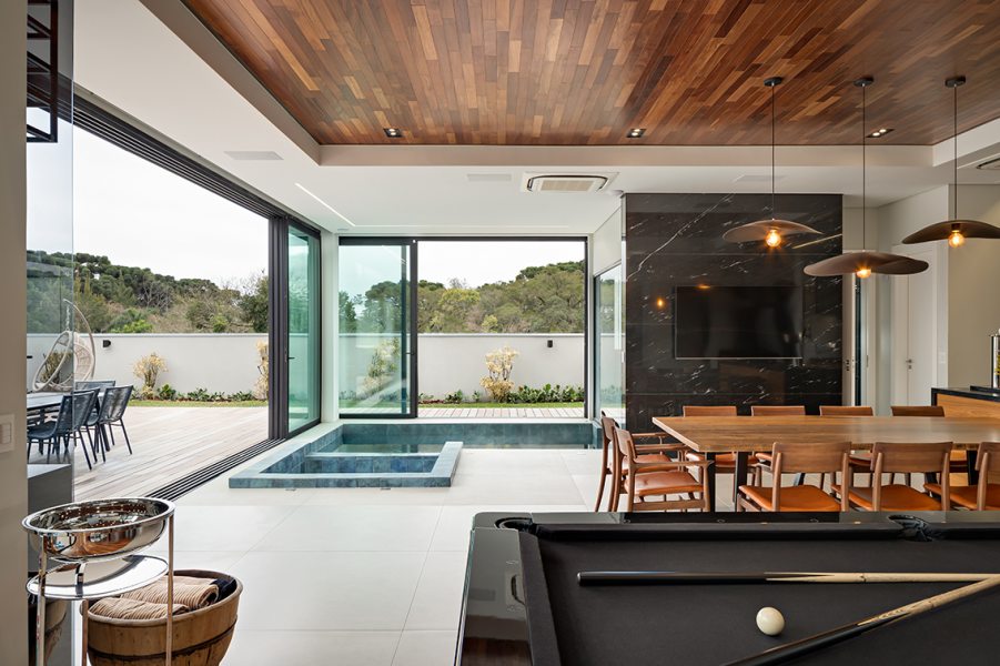 A ampla área social inclui espaço gourmet, sala de jogos, churrasqueira, sala de estar com lareira, piscina, sauna e cozinha gourmet. O layout integrado valoriza os momentos de lazer e convivência em família