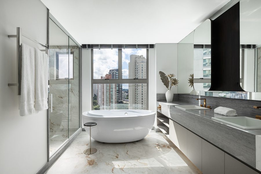 No banheiro, lavabos independentes, banheira e acabamentos neutros completam a proposta.