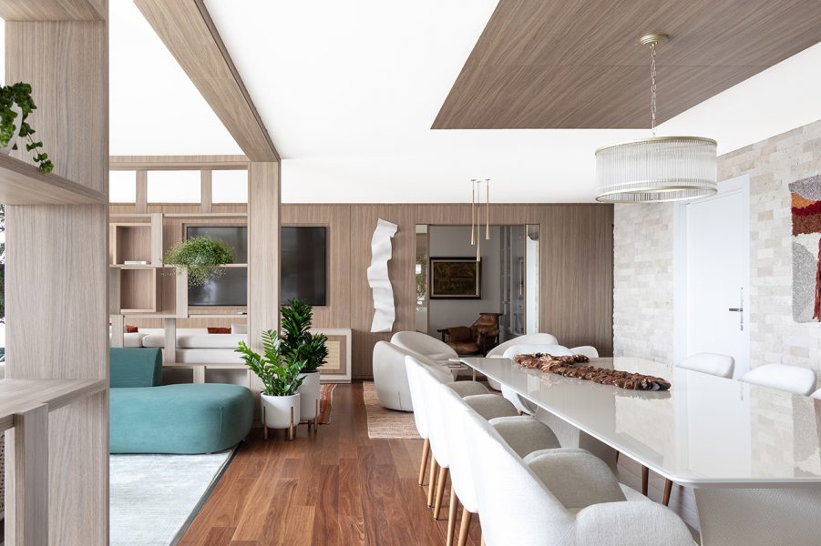 A integração entre sala de jantar, estar e varanda foi um dos primeiros gestos do projeto, definindo um layout fluido e contínuo. O piso de madeira reforça o acolhimento e a continuidade visual, enquanto o verde, presente no mobiliário e nos detalhes da decoração, atua como ponto de cor sobre a base neutra do apartamento.