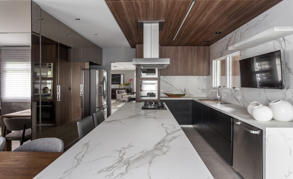 Todo o espaço é composto pela mescla harmoniosa de diferentes materiais. A madeira natural foi trabalhada no teto da cozinha e aparece também na mesa de jantar. Nas gavetas da cozinha e armários, madeira ebanizada e espelhos bronze. Para o luminotécnico, foram inseridos perfis como parte do teto de madeira, para uma melhor iluminação da bancada e áreas de trabalho Todo o espaço é composto pela mescla harmoniosa de diferentes materiais. A madeira natural foi trabalhada no teto da cozinha e aparece também na mesa de jantar. Nas gavetas da cozinha e armários, madeira ebanizada e espelhos bronze. Para o luminotécnico, foram inseridos perfis como parte do teto de madeira, para uma melhor iluminação da bancada e áreas de trabalho