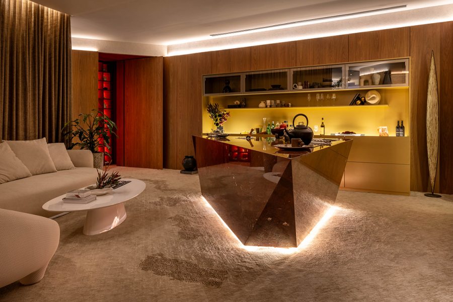 No Coração da Casa — Feu Singular: sala-ritual com bancada em mármore, luz indireta e tons terrosos e vermelhos profundos.