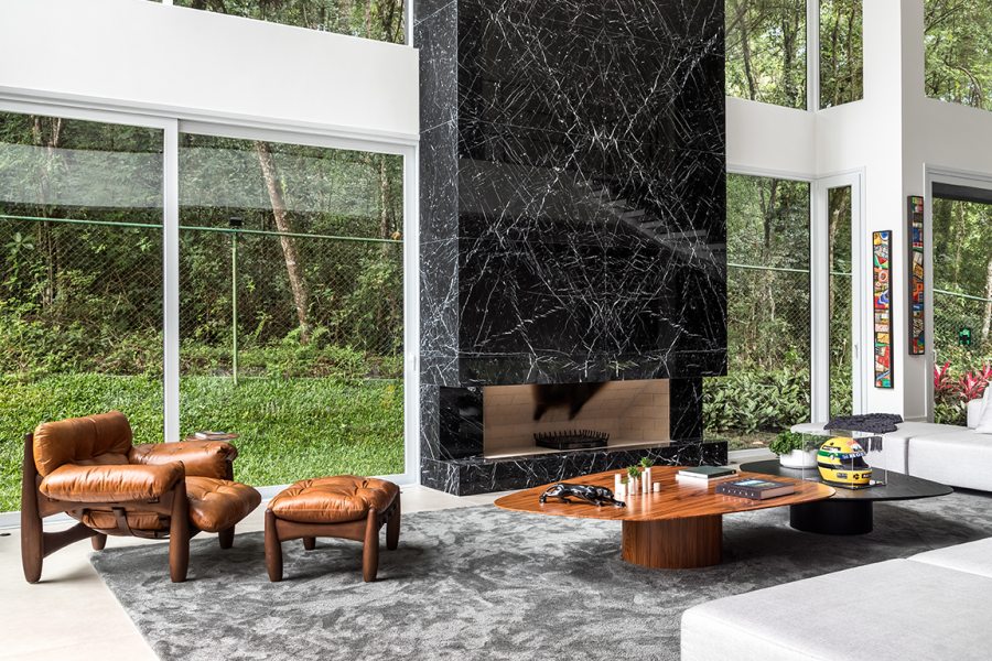 Da entrada principal é possível acessar o pavimento superior, através da escada helicoidal escultórica  ou circular pelo living com lareira. O tapete shaggy cinza é da Persépolis Tapetes.