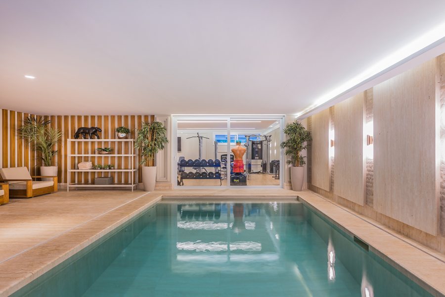Saúde em primeiro lugar: a academia integrada à piscina interna garante que os moradores mantenham as atividades físicas em dia em qualquer estação do ano. A iluminação indireta confere aspecto ainda mais convidativo aos elementos amadeirados e aos pisos e paredes de mármore natural.