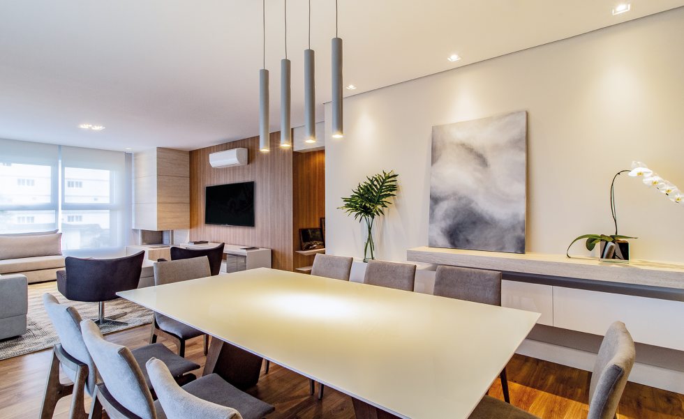 No living integrado com sala de jantar, o quarteto de pendentes minimalistas (Grey House) foi alinhado sobre a mesa, para uma iluminação que realça o mobiliário laca branca e vidro extra clear