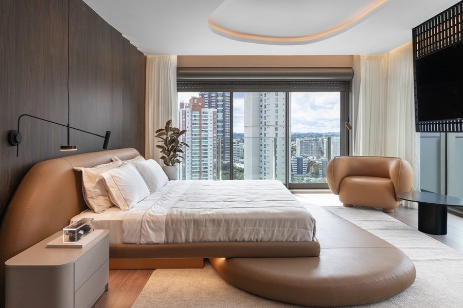 A suíte principal reúne dormitório, closet e banheiro em um conjunto contínuo e funcional. A cabeceira em tecido e a luz indireta reforçam a sensação de refúgio.