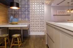A parede de cobogós brancos Recife DelFavero combina com a parede em ladrilhos hidráulicos, ambos da Revesttir, e proporciona uma transição suave entre a sala e a cozinha, em razão da transparência do revestimento.