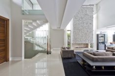 O design único da escada com guarda-corpo em vidro une os pavimentos esbanjando elegância. Aqui, é impossível não notar como a escolha do porcelanato Mineral Nude Polido (Portobello Shop) privilegia a incidência de luz natural e a reflete pela casa.