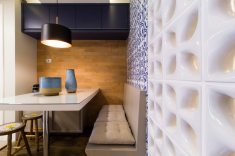 Na parede dos fundos, ladeando a mesa de jantar, a tonalidade terrosa do tijolo Toscana Palha (Revesttir) combina com armário superior em MDF azul escuro.
