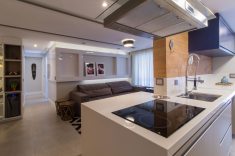 A bancada da cozinha, com cooktop e espaço para dois convidados sentados, é aberta para a sala de estar, aumentando a integração entre os espaços. 