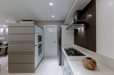 A bancada da cozinha foi trabalhada em Silestone branco Stelar. Atrás da coifa, painel em Silestone marrom Absoluto.